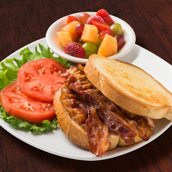 Eggbert's bacon sandwich with lettuce, tomato, and a side of fresh fruit.