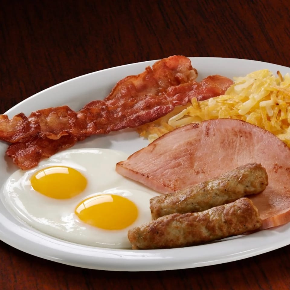 Eggbert's breakfast platter with two fried eggs, bacon, sausage links, ham, and hash browns.