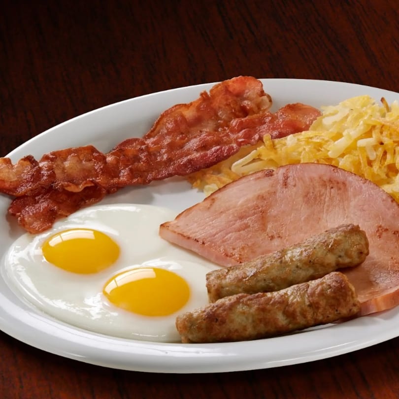 Eggbert's breakfast platter with two fried eggs, bacon, sausage links, ham, and hash browns.